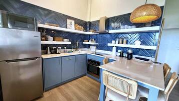 A modern kitchen with a refrigerator, stove, and sink. There are shelves above the counter with various kitchen items.