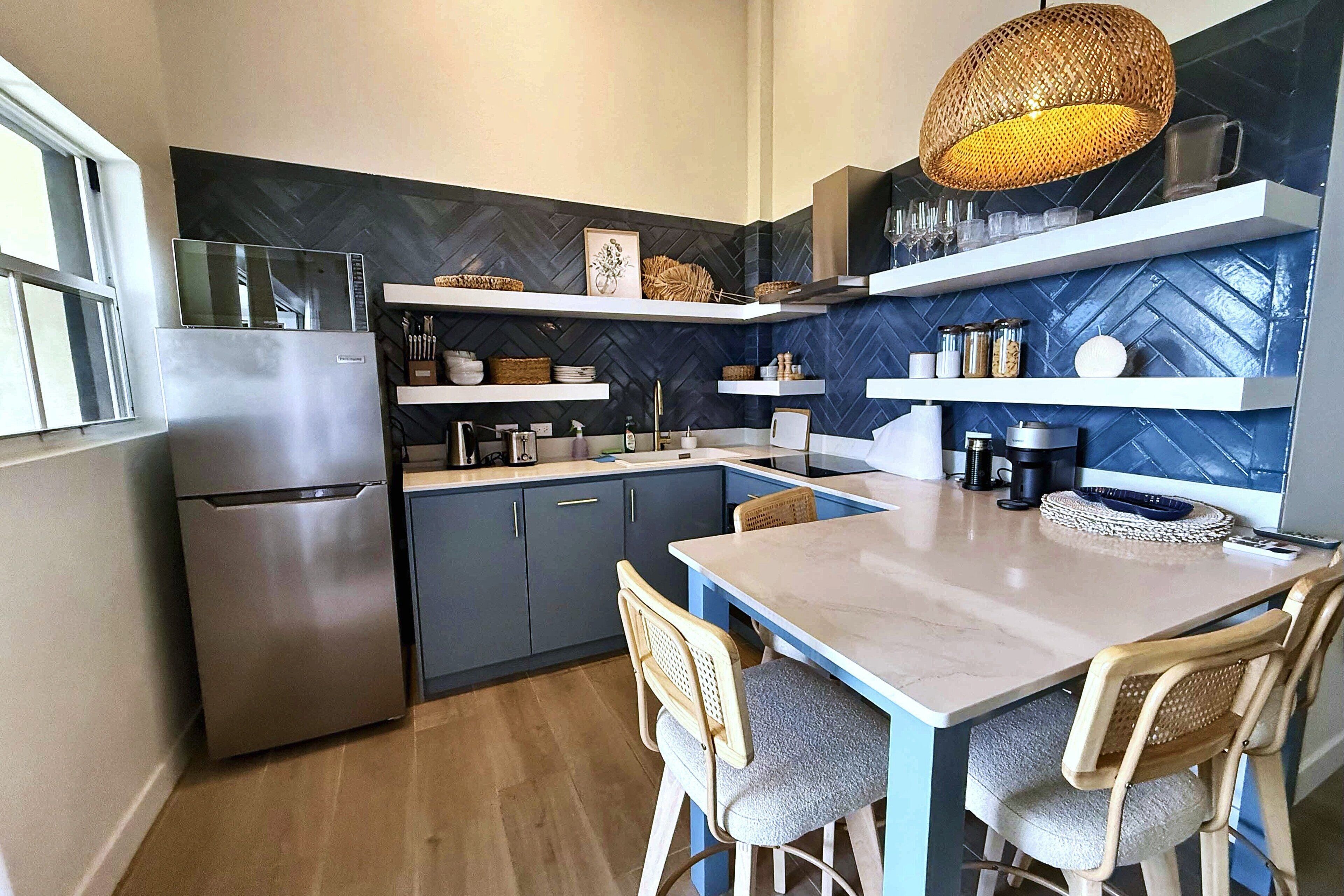 Una cocina compacta con refrigerador integrado, una mesa de comedor con sillas y una lámpara colgante.