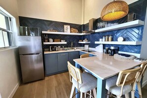 A compact kitchen with a built-in refrigerator, a dining table with chairs, and a hanging light fixture. - Lantana Sea La Vie - by Zenbreak (Weston)