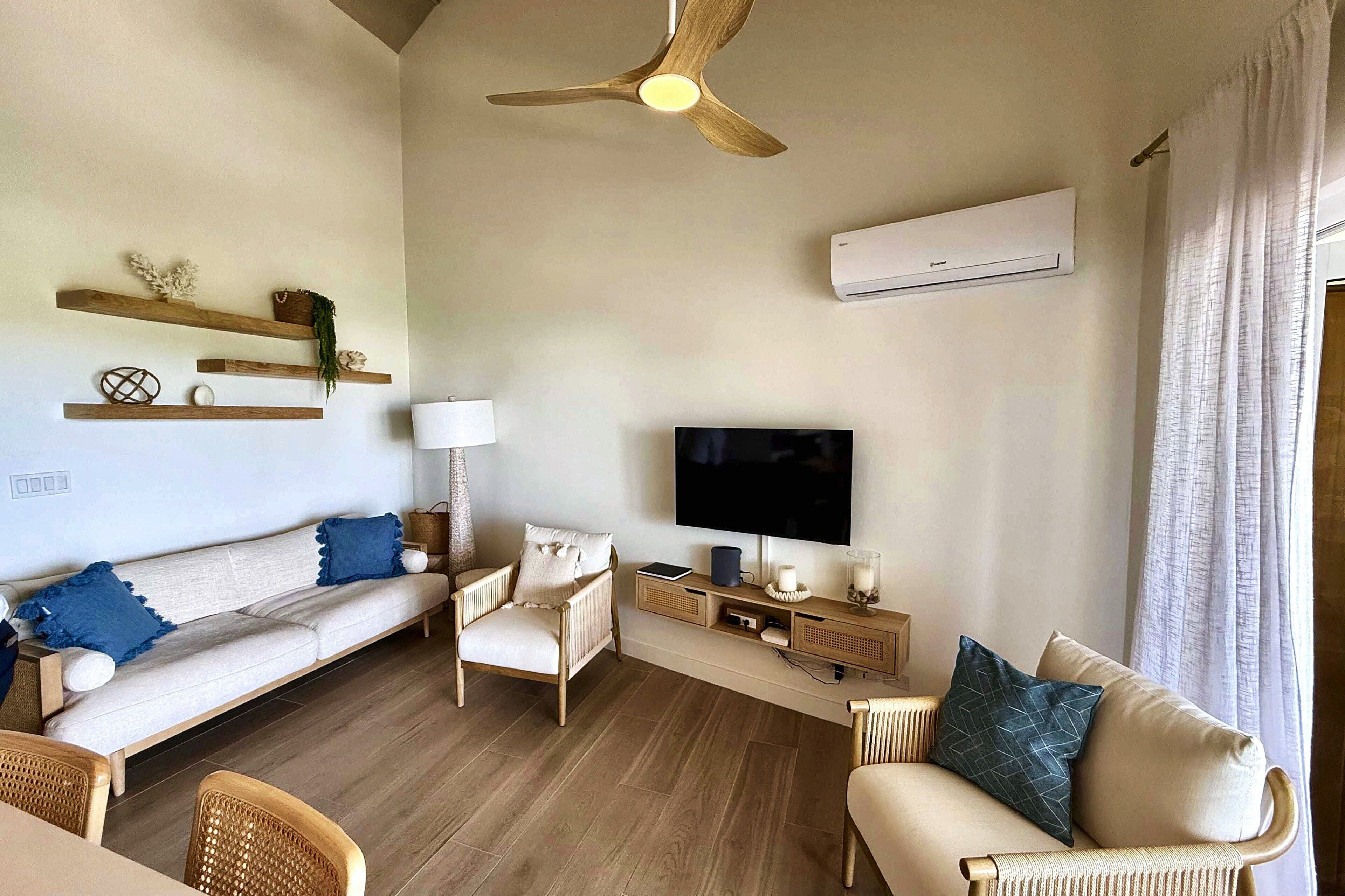 A modern living room with a sofa, chairs, a TV, and a ceiling fan.
