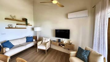 A modern living room with a sofa, chairs, a TV, and a ceiling fan.