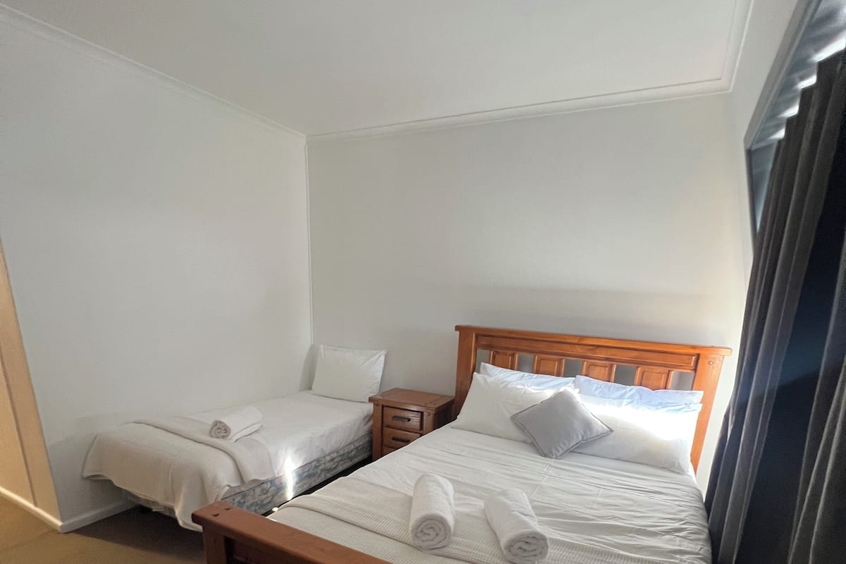 A hotel room with a wooden bed, a small wooden nightstand, a table, and a chair.