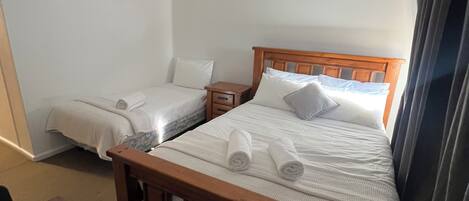 A hotel room with a wooden bed, a small wooden nightstand, a table, and a chair.