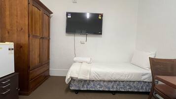 Una habitación pequeña y sencilla con cama, un armario de madera, televisor montado en la pared y una mesita.