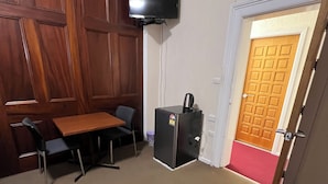 Ein Zimmer mit einer Holzvertäfelung, einem Tisch mit Stühlen, einem kleinen schwarzen Kühlschrank und einem an der Wand montierten Fernseher.