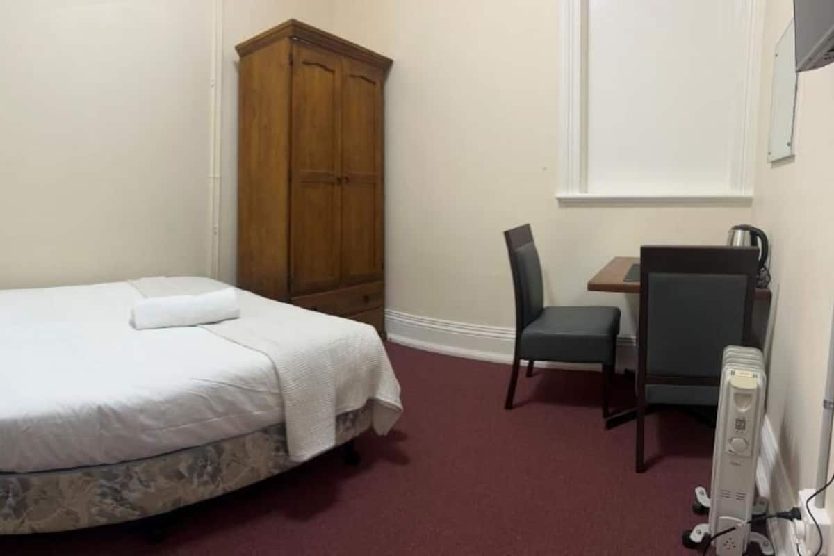 A bedroom with a bed, a wardrobe, a desk with a chair, and a radiator.