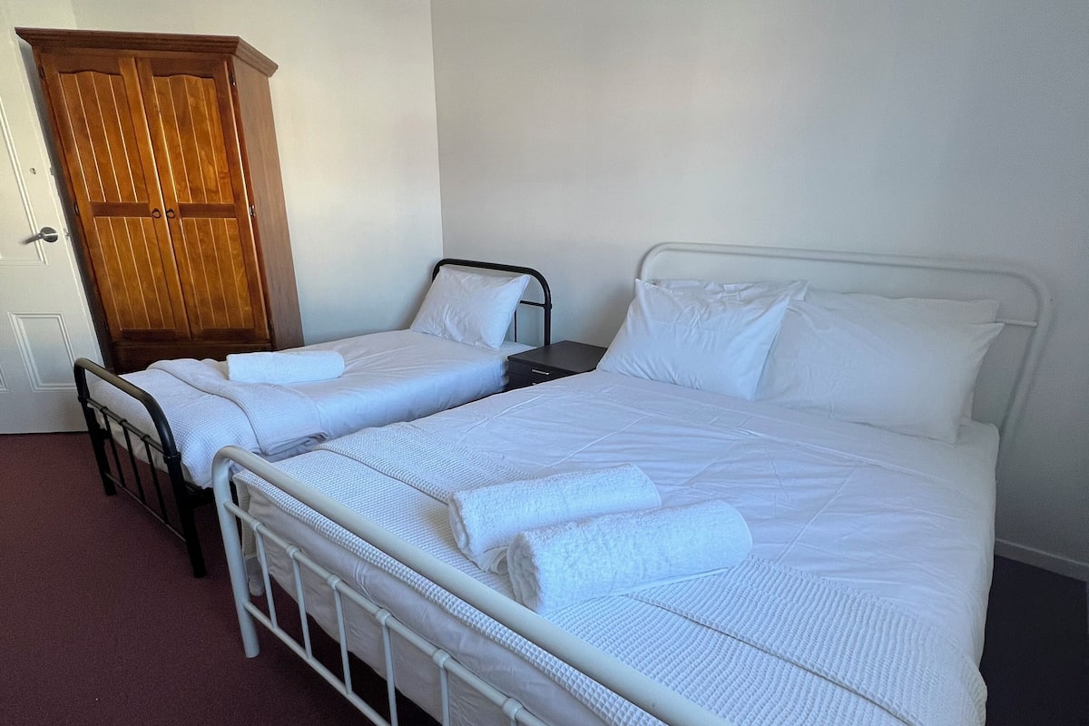 A room with two single beds, a wooden wardrobe, and a door.