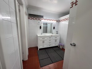 Un baño con paredes de azulejos blancos, un tocador blanco con espejo y suelo de baldosas rojas.