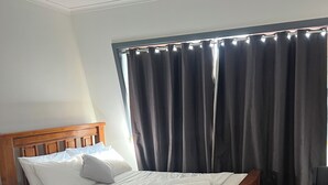 Ein Hotelzimmer mit einem hölzernen Bett, einem Nachttisch, einem Sessel und einem großen Fenster mit Vorhängen.