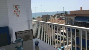 A balcony with a white railing, a table with a candle and a cup, and a view of the sea and buildings in the background. - Apartment very seafront beachfront Pobla Farnals beach (La Pobla de Farnals)