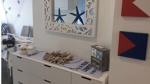 Une pièce comprenant une commode blanche, un miroir doté d’un cadre décoratif et un mur orné d’œuvres d’art abstraites.