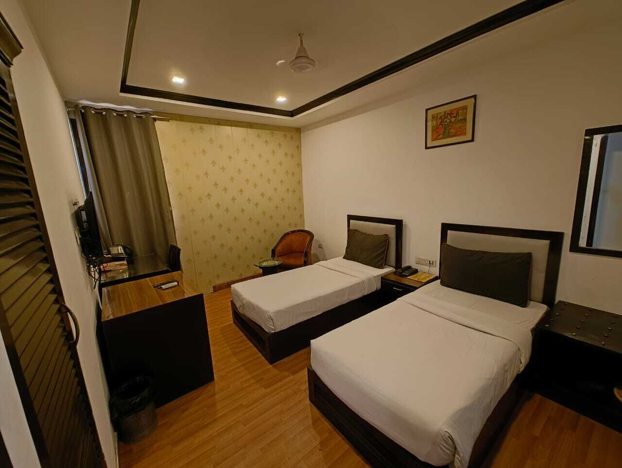 Une chambre d’hôtel avec deux lits, un bureau, une chaise, une petite table et un ventilateur de plafond.