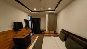 A hotel room with a bed, a desk, a television, and a window with curtains. - Hotel Veer Palace (New Delhi)