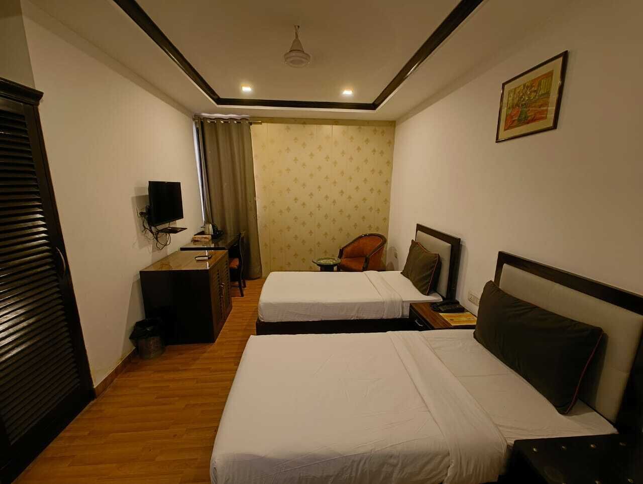 Ein Hotelzimmer mit zwei Betten, einem Schreibtisch, einem Stuhl, einem Fernseher und einem Deckenventilator.