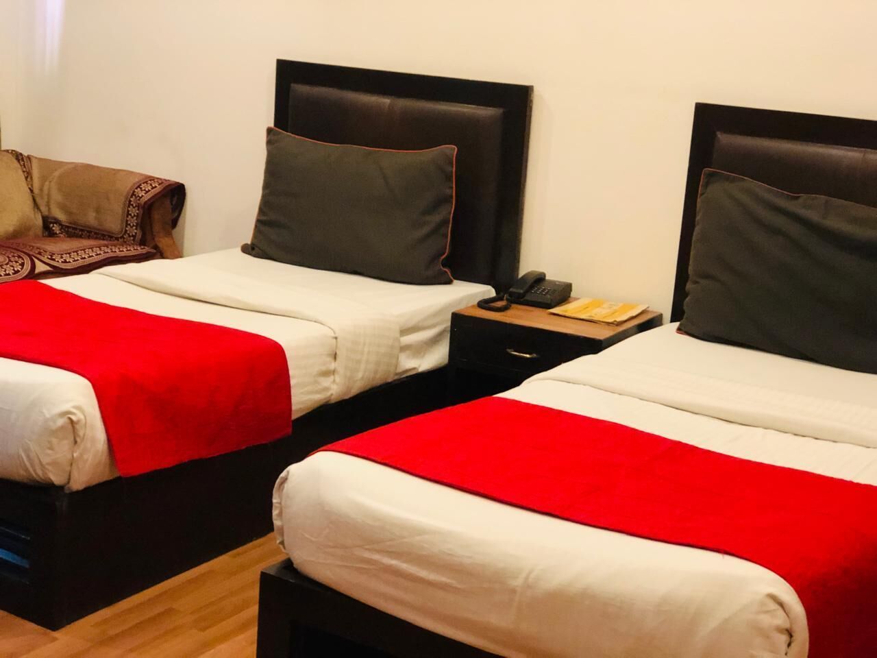 Zwei Betten mit roter und weißer Bettwäsche, eine braune Tagesdecke und ein Nachttisch aus Holz mit einem Telefon und einem Buch.