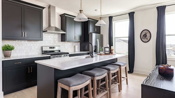 A modern kitchen with dark cabinetry, a large island with bar stools, stainless steel appliances, and pendant lighting.