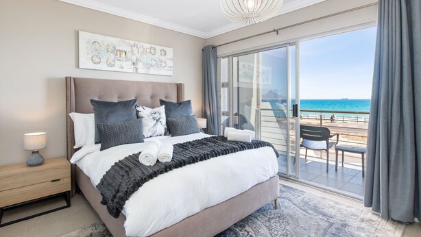 A bedroom with a large bed, a nightstand, a ceiling light, and a view of the beach through a sliding glass door. - 9 On The Waves (Cape Town)