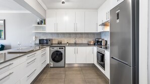 A modern kitchen with white cabinets, stainless steel appliances, a washing machine, and a large refrigerator. - 9 On The Waves (Cape Town)
