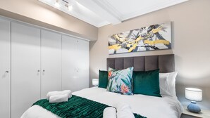 A hotel room with a large bed, a headboard with decorative pillows, a green throw blanket, and a painting on the wall. - 9 On The Waves (Cape Town)