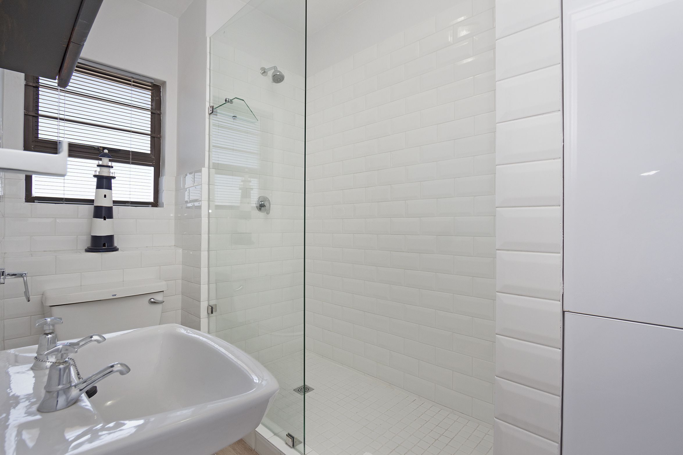 Une salle de bain moderne avec une douche à parois de verre, des murs recouverts de carreaux blancs et un lavabo avec un robinet.