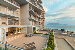 A modern multi-story hotel with balconies, outdoor seating, and a view of the sea. - Horizon Bay 103 (Cape Town)