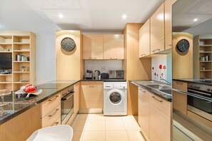 A modern kitchen with wooden cabinets, a built-in washing machine, and a clock on the wall. - Horizon Bay 103 (Cape Town)