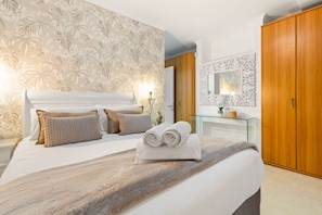 A bedroom with a large bed, a glass bedside table, a wooden wardrobe, and a decorative mirror. - Horizon Bay 103 (Cape Town)