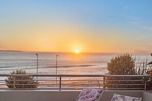 A sunset view from a balcony overlooking the sea, with a railing and some greenery in the foreground. - Horizon Bay 103 (Cape Town)