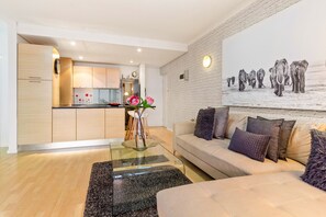 A modern living room with a glass coffee table, a beige sofa with cushions, and a large wall art of elephants. - Horizon Bay 103 (Cape Town)