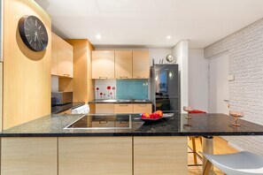 A modern kitchen with wooden cabinets, a black countertop, a built-in stove, and a stainless steel refrigerator. - Horizon Bay 103 (Cape Town)
