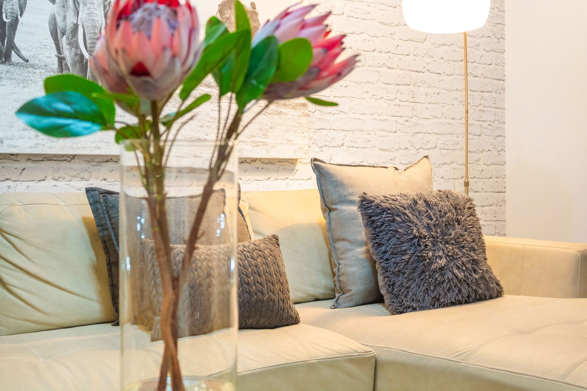 A living room with a beige sofa, a vase with flowers, and a white brick wall.