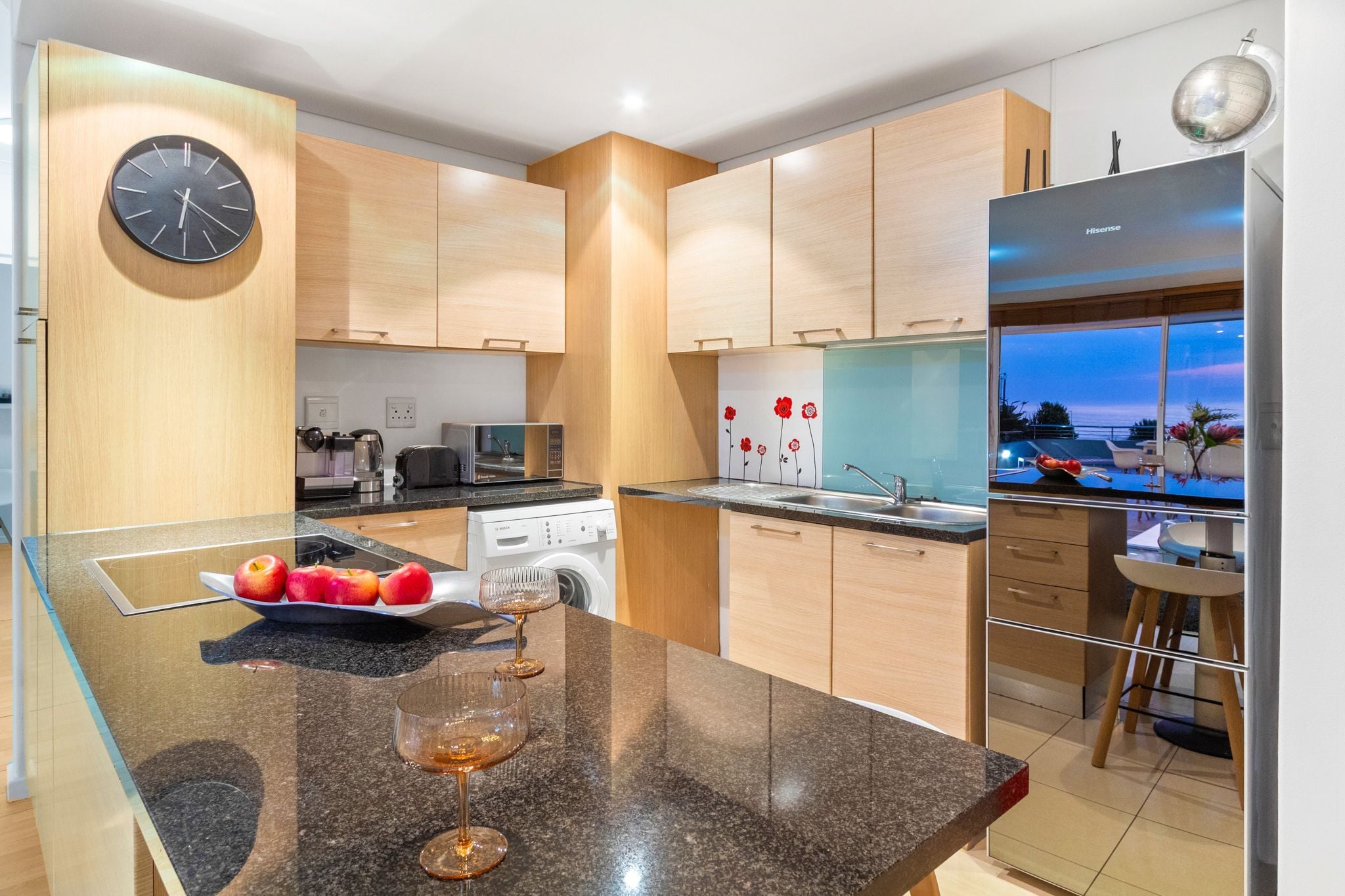 A modern kitchen with wooden cabinets, a built-in oven, a dishwasher, and a large window overlooking a scenic view.