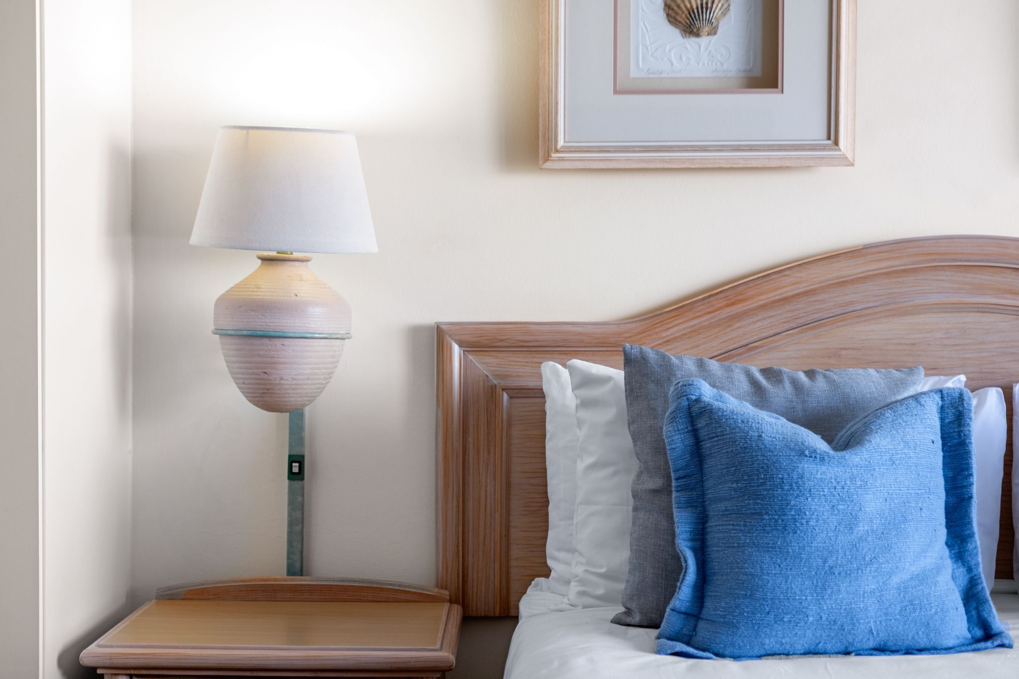Un letto rifatto con cura, una testiera in legno, un comodino con una lampada e un quadro appeso al muro.