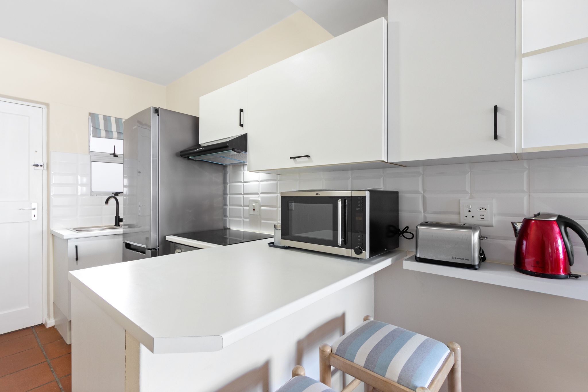 A modern kitchen with white cabinets, a stainless steel refrigerator, a microwave, a toaster, and a red kettle.