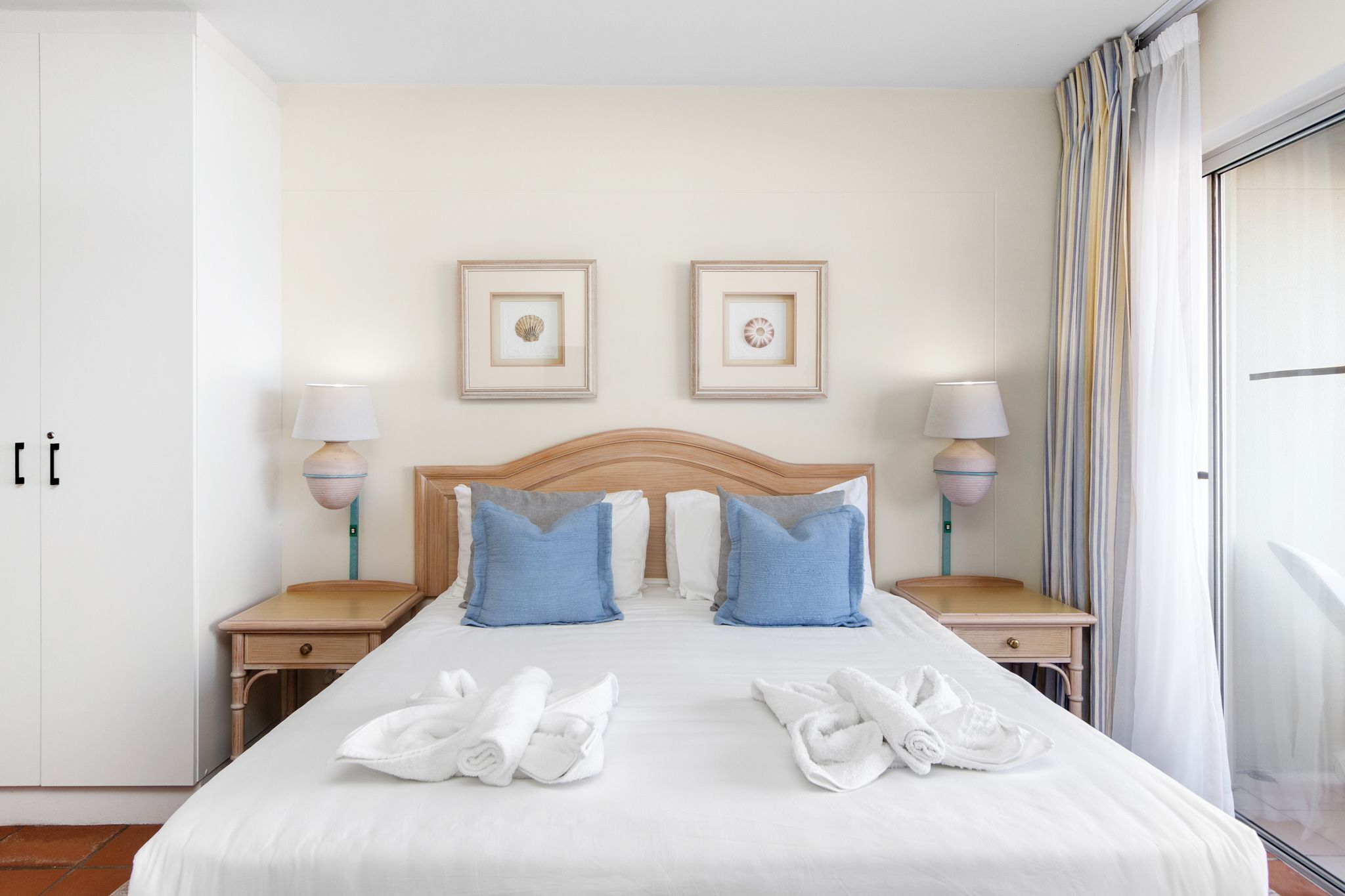 Camera d'albergo con un letto grande, due comodini, una testiera in legno e due quadri appesi alla parete.