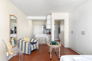 A compact hotel room with a kitchenette, a striped sofa, a small table, and a bed. - Sea Spray A410 (Cape Town)