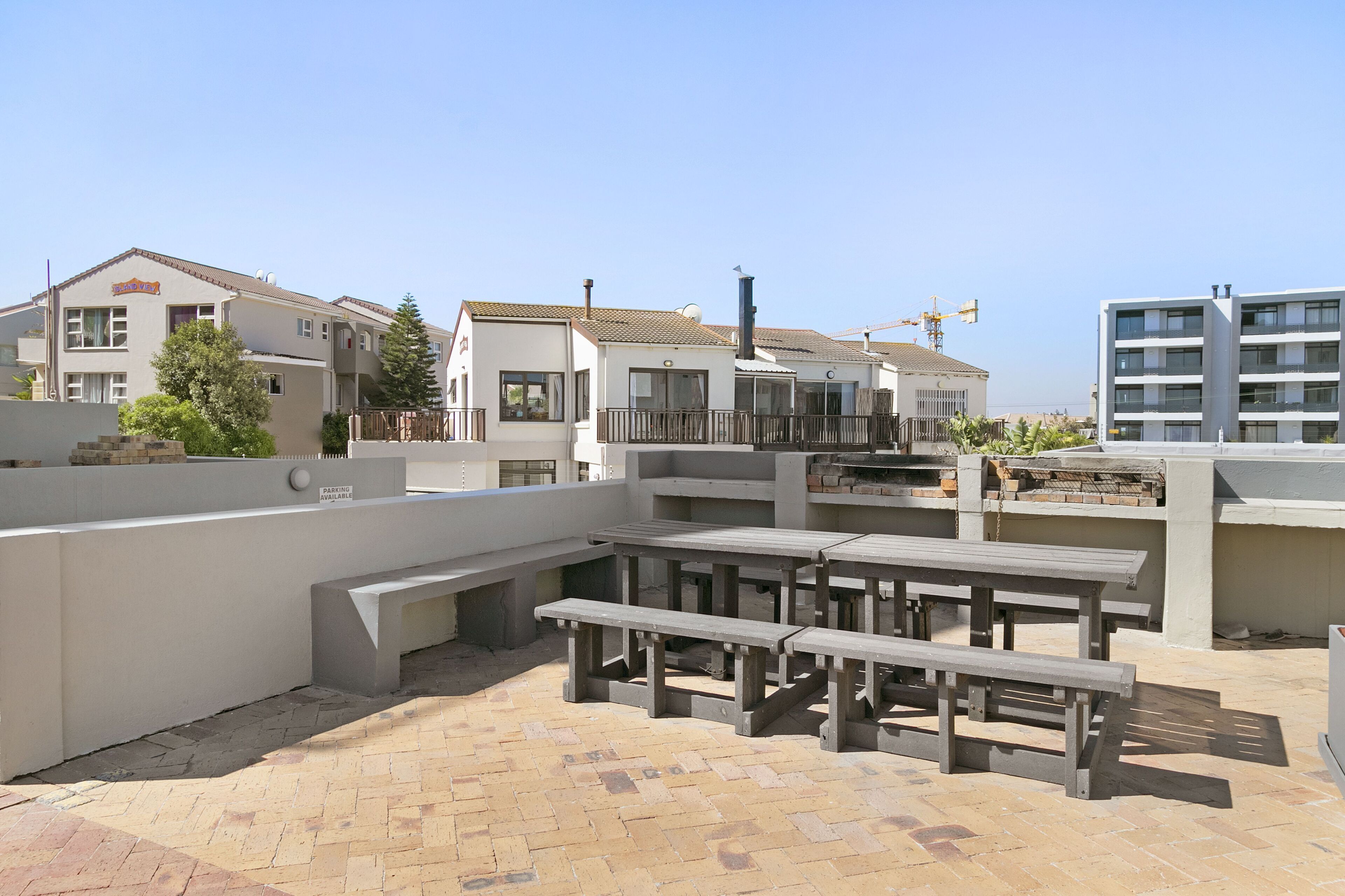 A rooftop patio with picnic tables, a barbecue area, and a view of surrounding buildings.