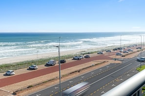A coastal road with a red bike lane, a beach, and parked cars.