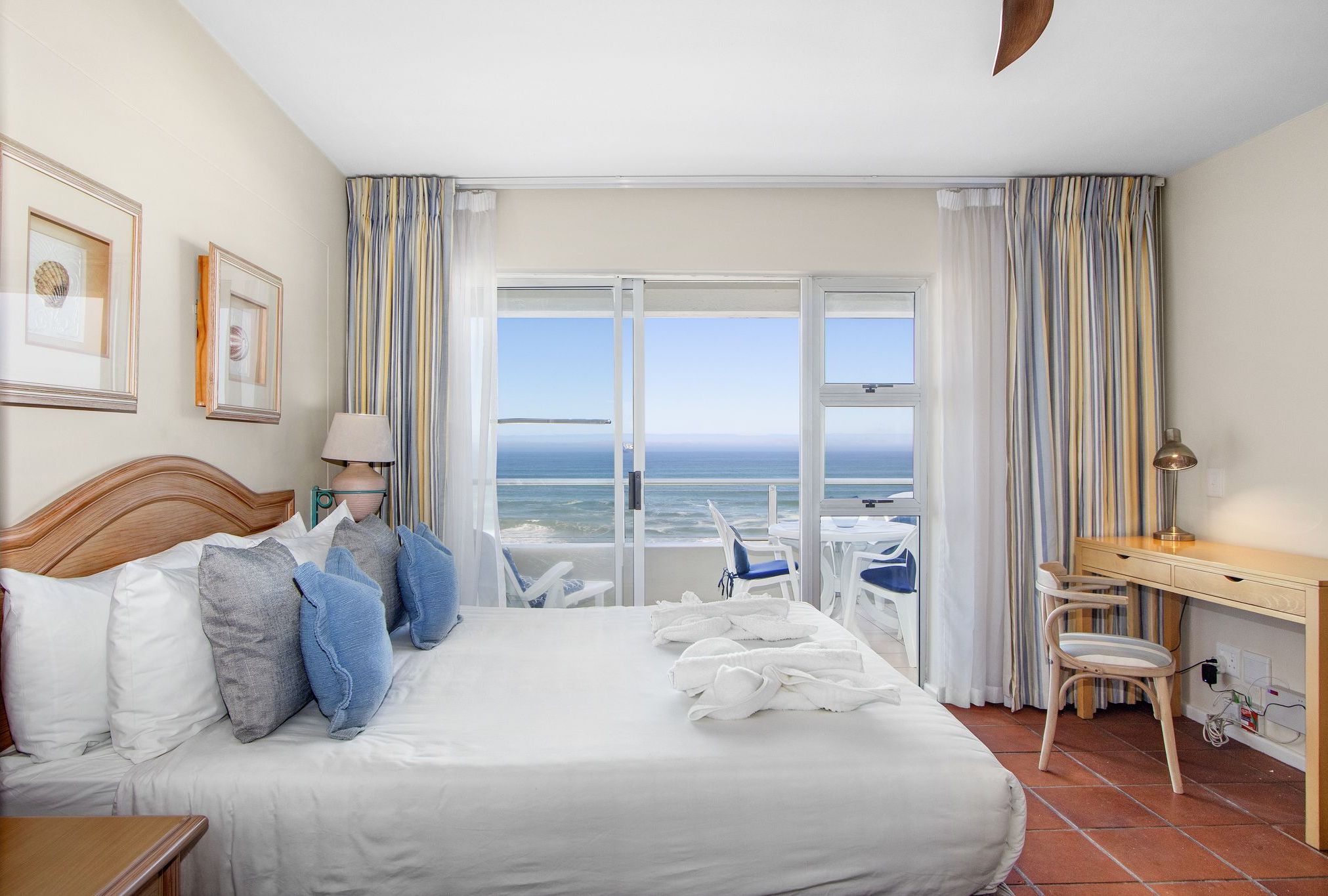 A hotel room with a large bed, a desk, a chair, and a view of the ocean.