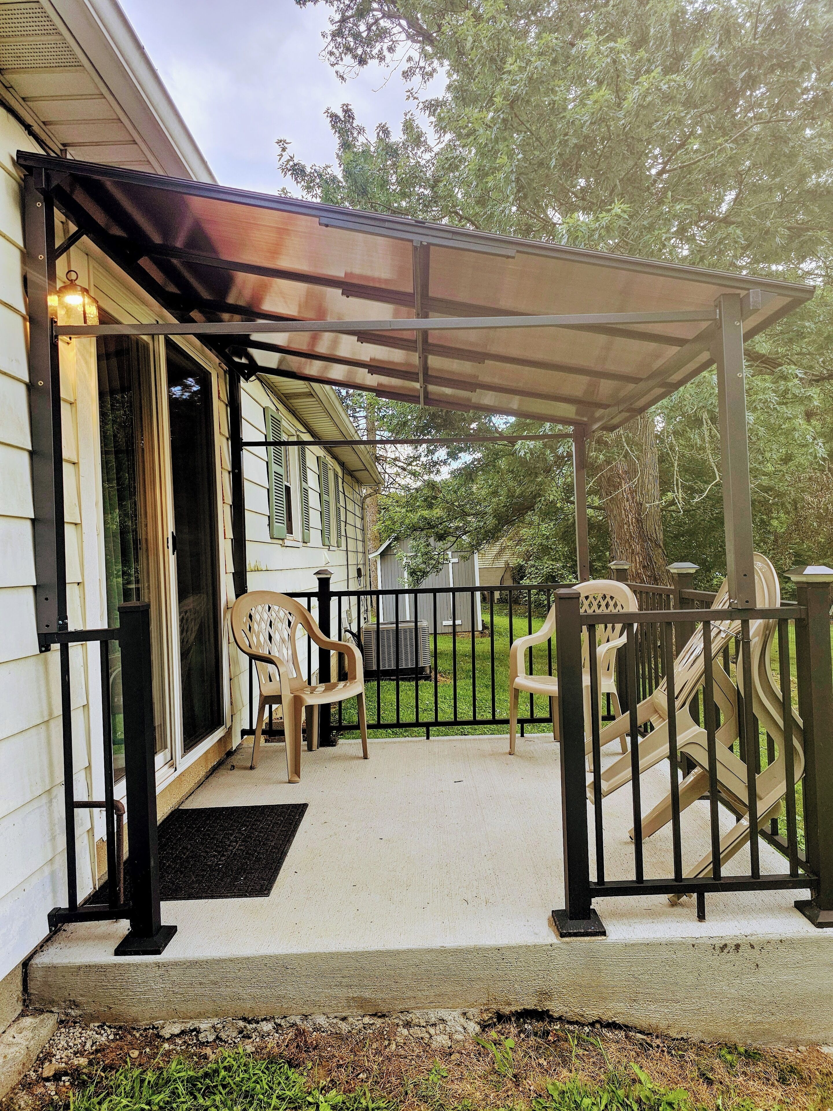 A covered porch with a metal railing, a sliding glass door, and a small outdoor seating area with plastic chairs.