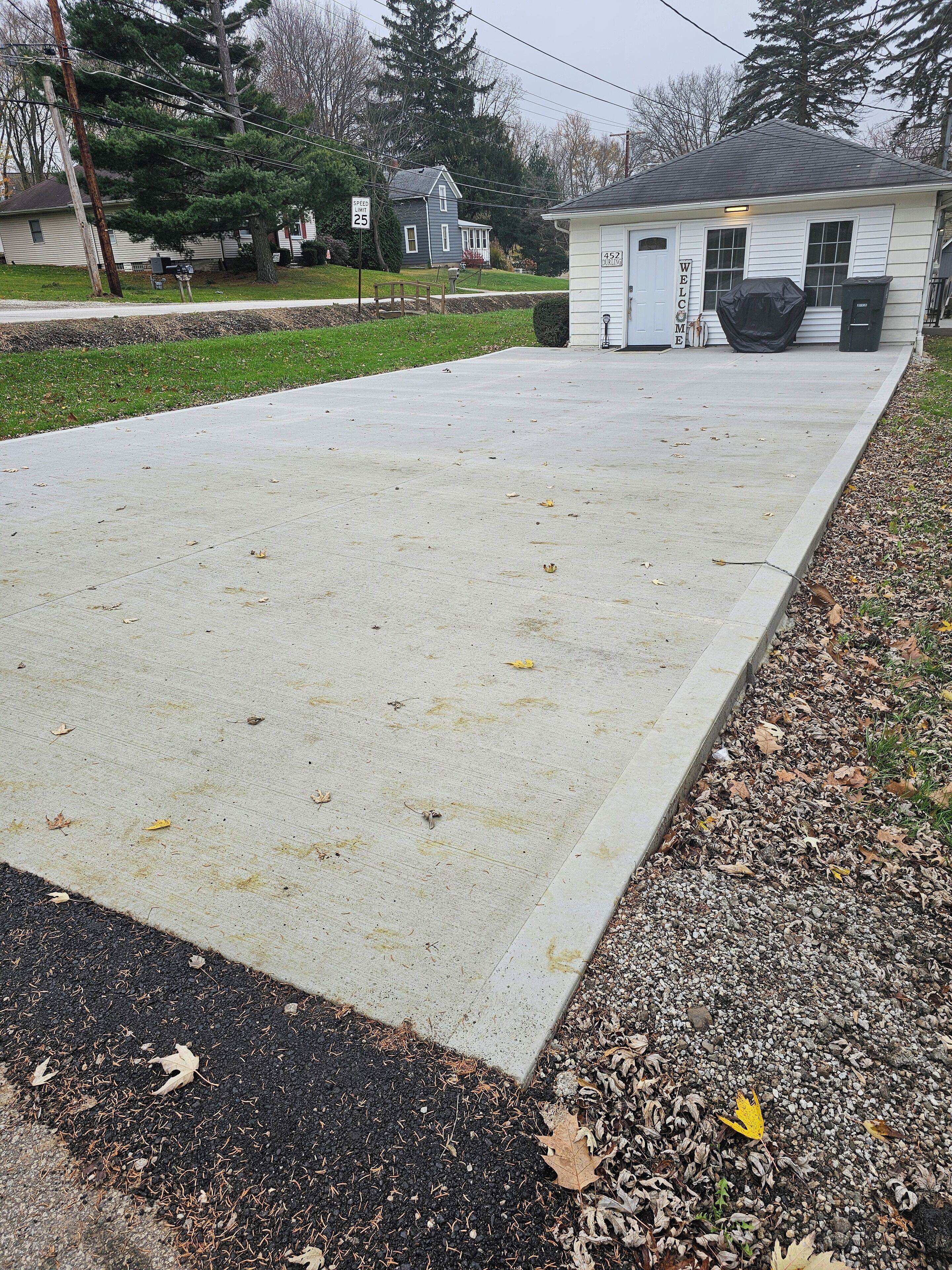 A concrete driveway leading to a small building with a 'WELCOME' sign.