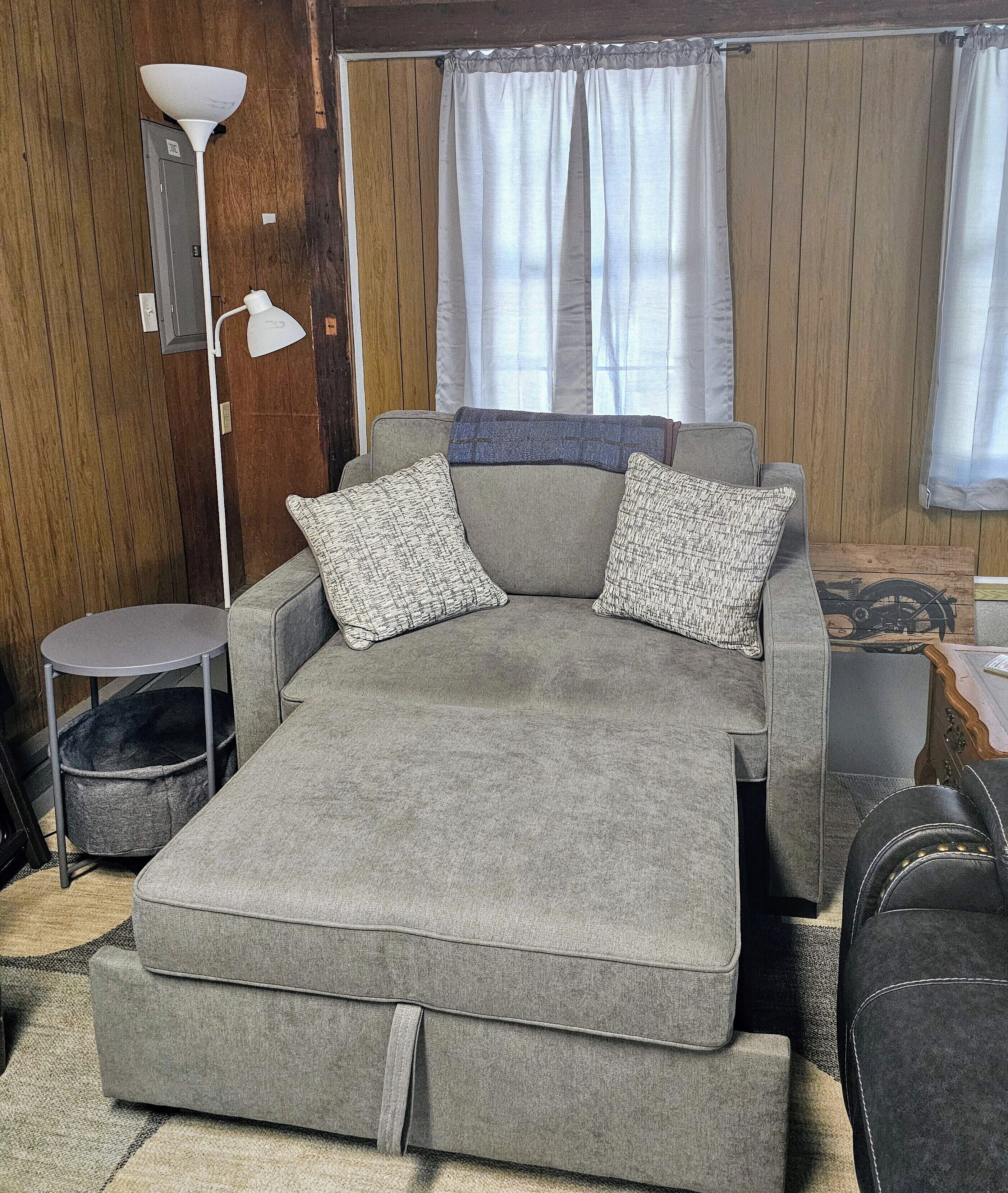 A grey sofa with two patterned pillows, a small round table, and a floor lamp.