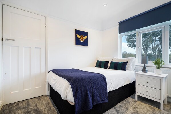 A bedroom with a bed, a nightstand, a window, and a door.
