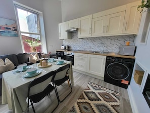 A modern kitchen with white cabinets, a built-in oven, a washing machine, and a dining area with a table set for four. - Top Location - Newly Refurbed 2BD, Sleeps 6 W/Loft (Cork)
