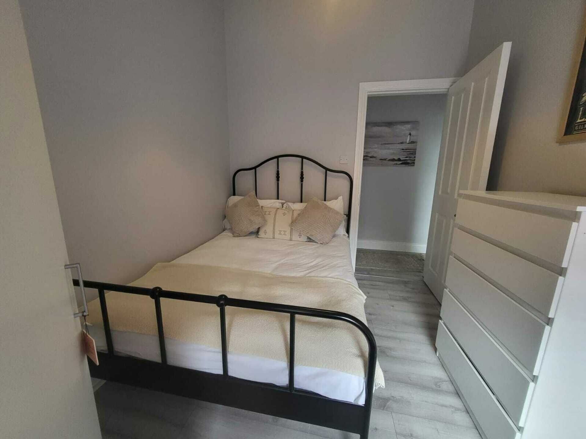 A narrow room with a single bed, a dresser, and a door leading to another room.