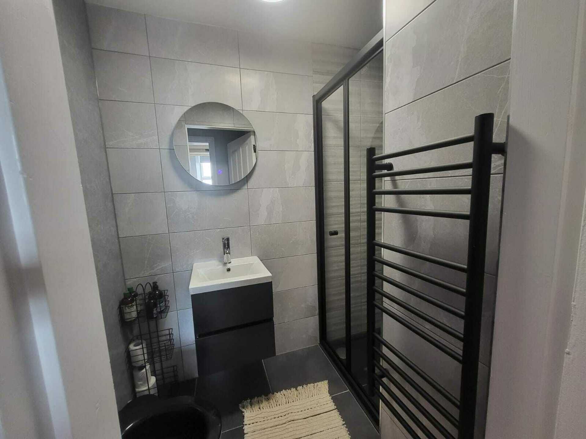 A compact bathroom with a white sink, a mirror, and a black towel rack.