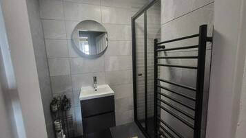 A compact bathroom with a white sink, a mirror, and a black towel rack.