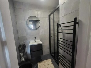 Une petite salle de bain avec un lavabo blanc, un miroir et un porte-serviettes noir.