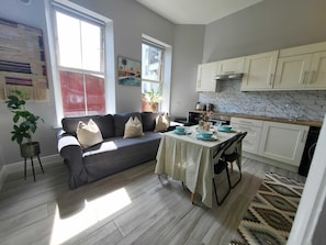 A modern living room with a sofa, a dining table set for four, and a kitchen with white cabinets and a marble backsplash. - Top Location - Newly Refurbed 2BD, Sleeps 6 W/Loft (Cork)