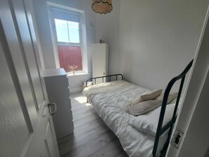 Une petite chambre avec un lit simple, une fenêtre, une armoire et une porte.